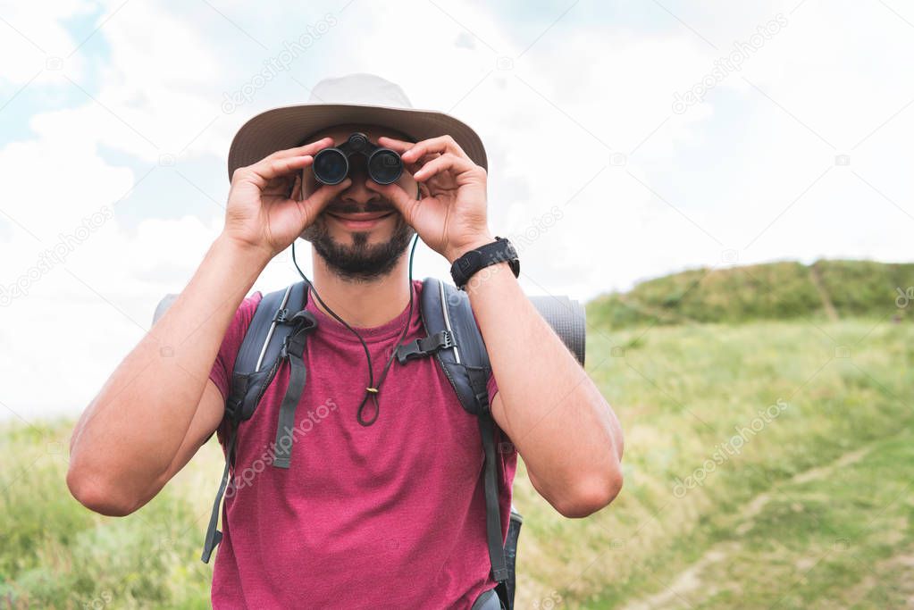 male tourist in hat with backpack looking in binoculars