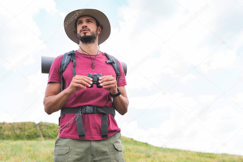 traveler in hat with backpack holding binoculars