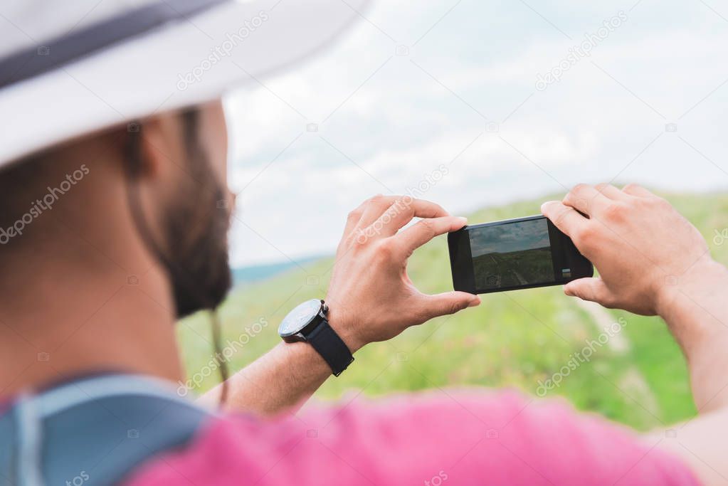 tourist with backpack taking photo on smartphone on green meadow