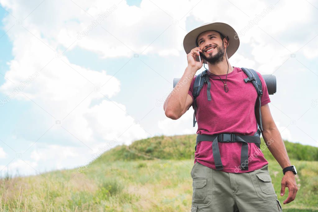 traveler with backpack talking on smartphone on summer meadow