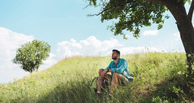 handsome traveler with backpack sitting on green summer meadow clipart