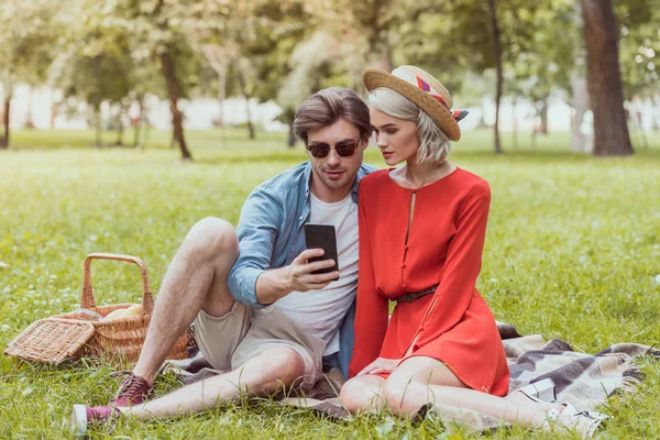 夫妇坐在毯子在公园和使用智能手机 — 图库照片