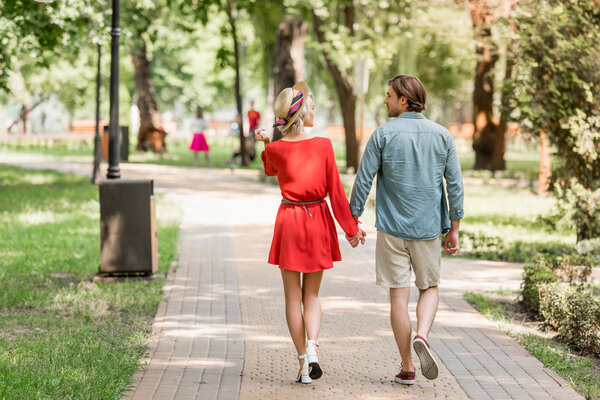 back view of girlfriend and boyfriend walking together in park and looking at each other