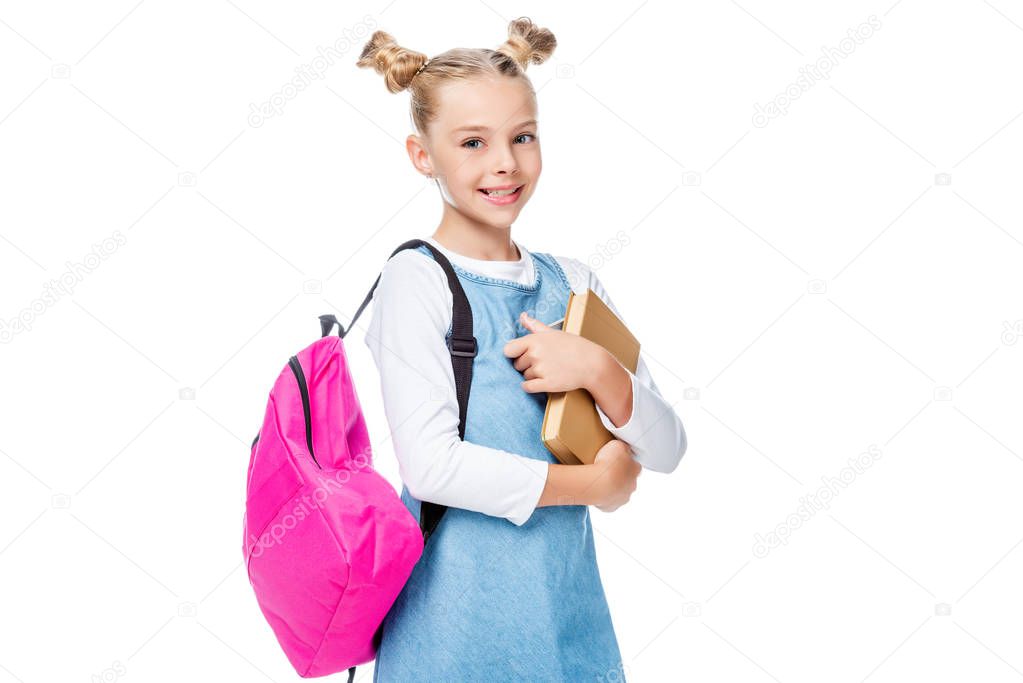smiling schoolchild with pink backpack holding books and looking at camera isolated on white