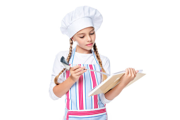 schoolchild in costume of chef reading recipe book isolated on white