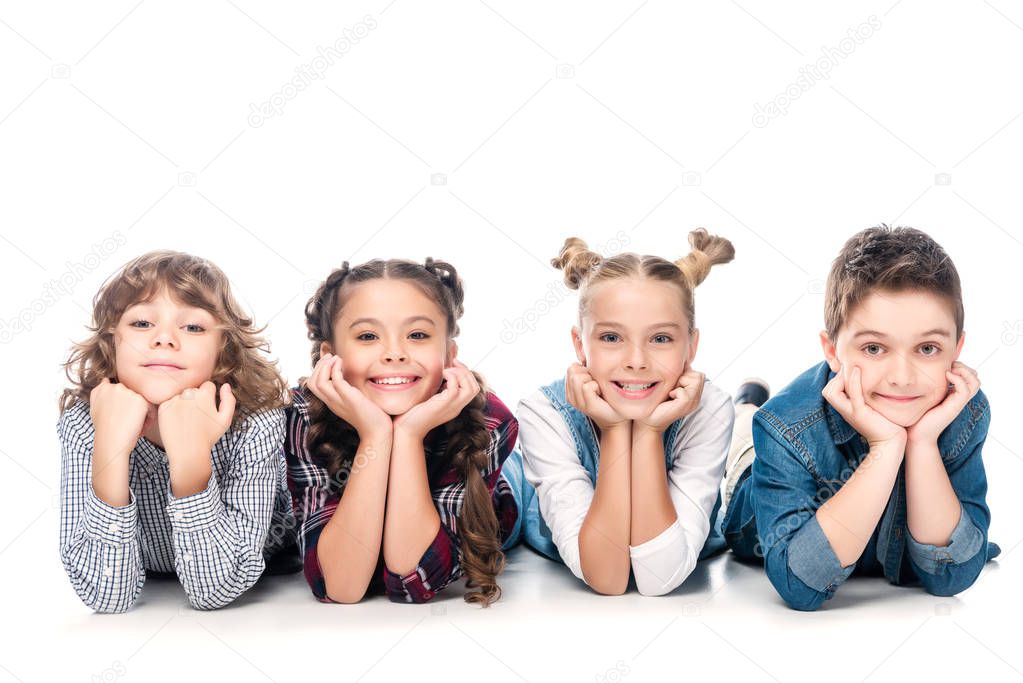 smiling classmates lying and resting chins on hands isolated on white