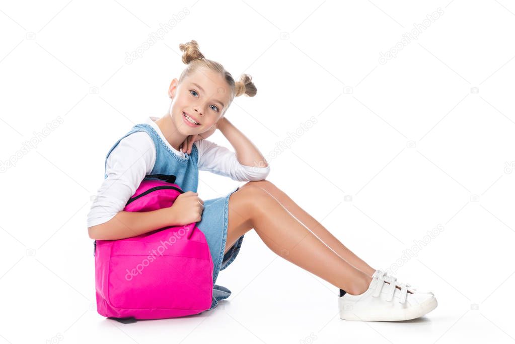 schoolchild sitting with pink backpack and looking at camera isolated on white