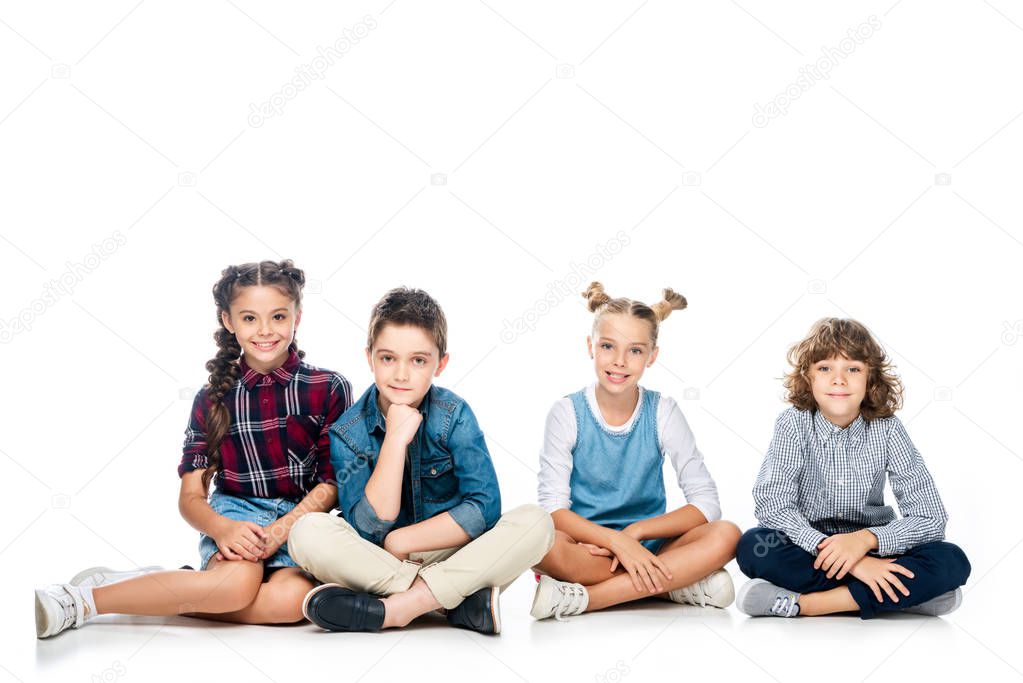 four schoolchildren sitting and looking at camera isolated on white