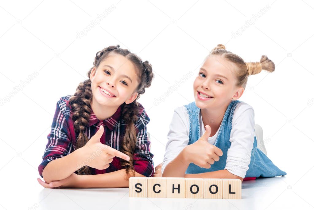 schoolchildren showing thumb up to wooden cubes with word school isolated on white