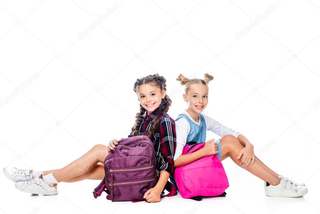 schoolchildren sitting with backpacks and looking at camera isolated on white 