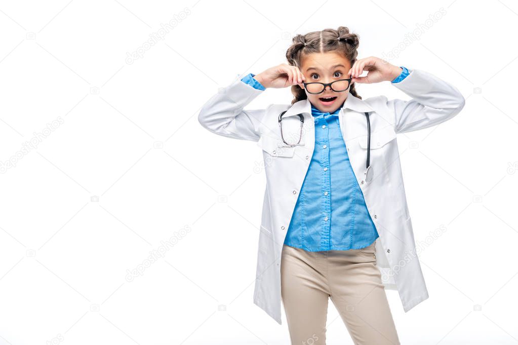 surprised schoolchild in costume of doctor looking above glasses isolated on white