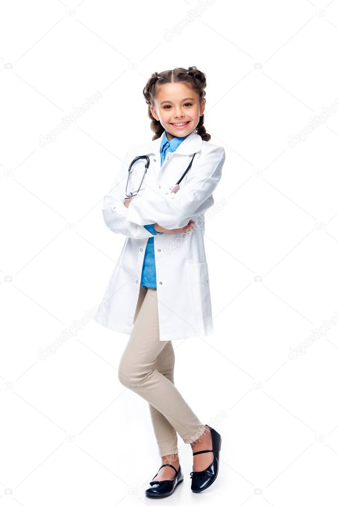 smiling schoolchild in costume of doctor standing with crossed arms isolated on white