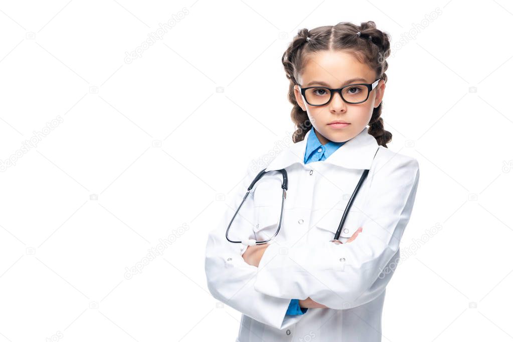 serious schoolchild in costume of doctor standing with crossed arms isolated on white