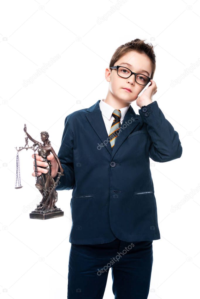 schoolboy in costume of lawyer holding themis statue and talking by smartphone isolated on white