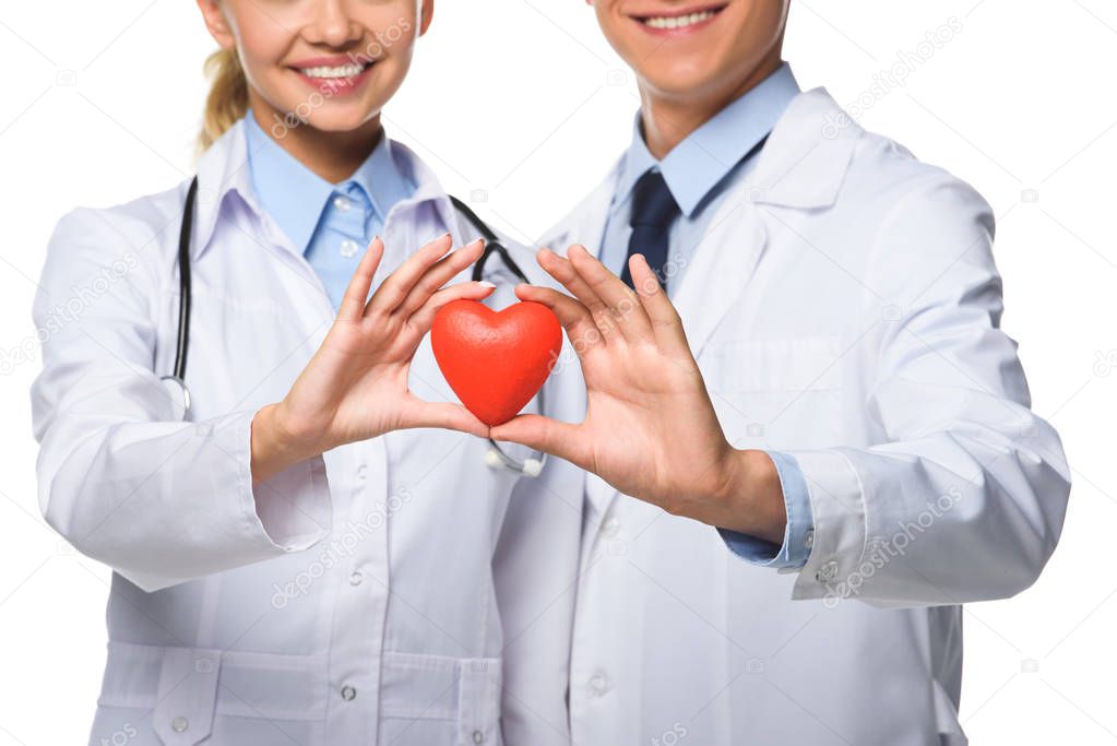 cropped view of two doctors in white coats holding red heart, isolated on white