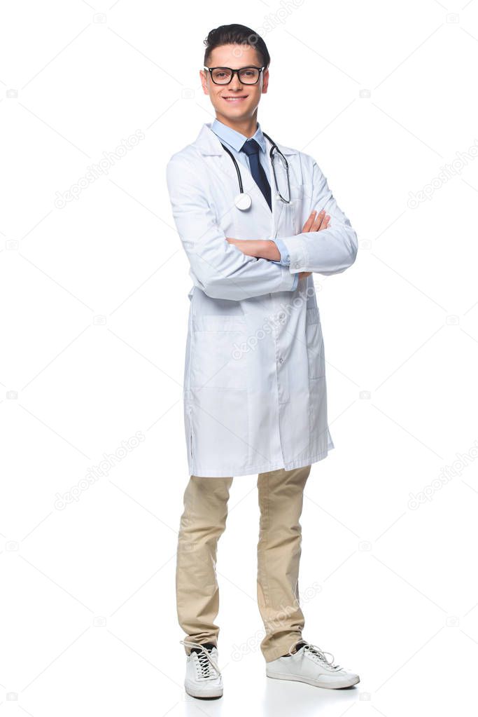happy young doctor with crossed arms looking at camera isolated on white