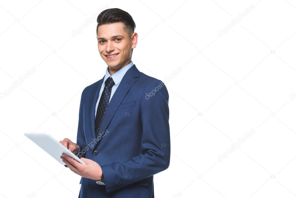 happy young businessman in stylish blue jacket using tablet and looking at camera isolated on white