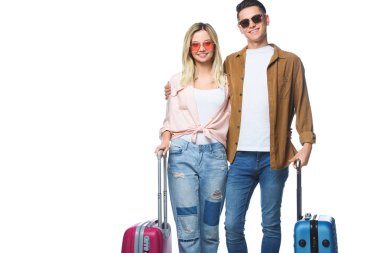 young smiling couple with suitcases looking at camera isolated on white clipart