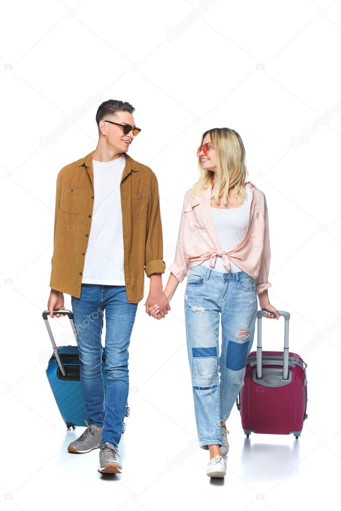 young travelling couple holding hands and walking with suitcases isolated on white