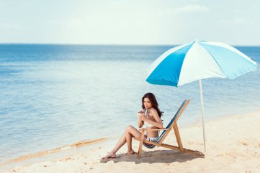 bikini içme Hindistan cevizi plaj şezlong deniz kenarında güneş şemsiyesi altında kokteyl genç kadın
