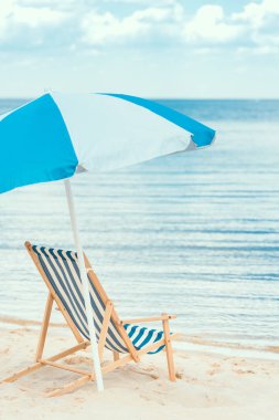 blue sun umbrella and beach chair on seaside in summer clipart