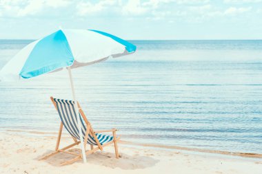 sun umbrella and beach chair on sandy shore near the sea clipart