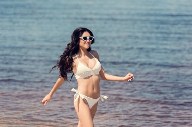 mutlu kadın güneş gözlüğü ve denize yakın çalışan beyaz bikini  