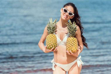 bikini ve taze ananas denize yakın tutarak güneş gözlüğü güzel gülümseyen kadın