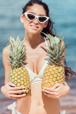 gülümseyen kız bikini ve taze ananas denize yakın tutarak güneş gözlüğü