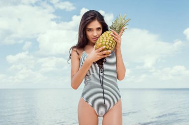Genç esmer kadın deniz kenarında ananas ile yaz aylarında poz mayo