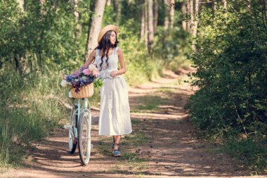 Bisiklet ve çiçeklerle parkta hasır sepet içinde yürüyüş beyaz elbiseli kız