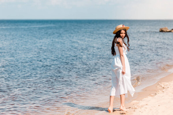 young woman in straw hat and white dress walking on beach