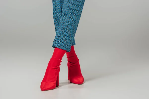 cropped image of female models legs in red stylish boots on grey background