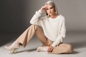 attractive fashionable woman posing in white trendy sweater, beige pants and autumn heels, on grey 