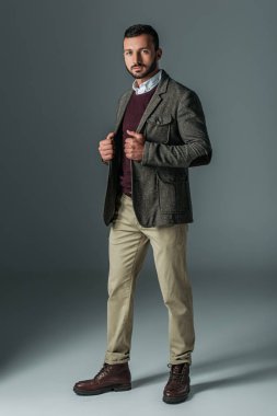 handsome male model posing in beige pants and tweed jacket, on grey clipart