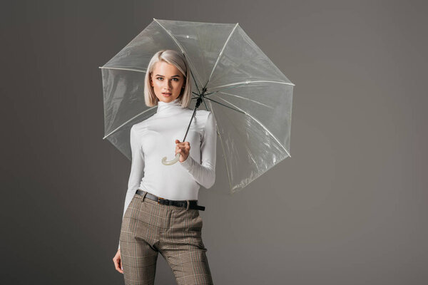 elegant model in white turtleneck with transparent umbrella, isolated on grey