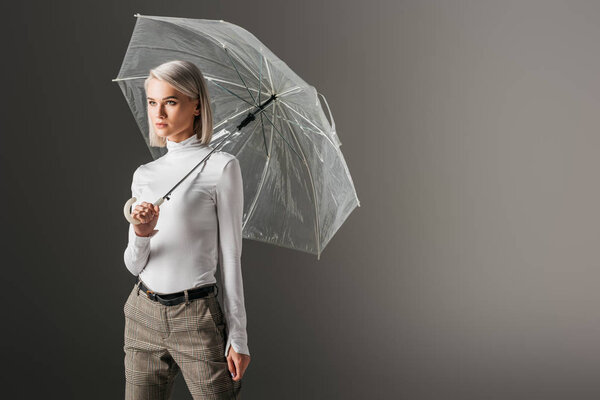 attractive girl in white turtleneck posing with transparent umbrella, isolated on grey