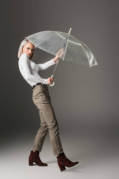 confused girl in white turtleneck with transparent umbrella, on grey