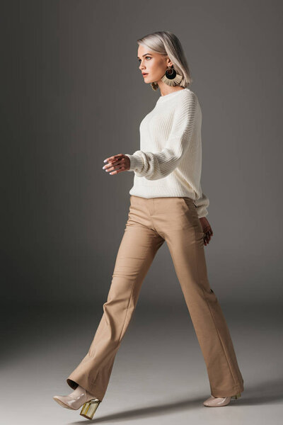 fashionable girl walking in beige pants and white sweater, on grey
