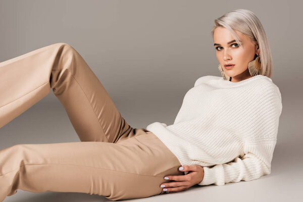 elegant blonde woman lying in white sweater and beige pants, on grey