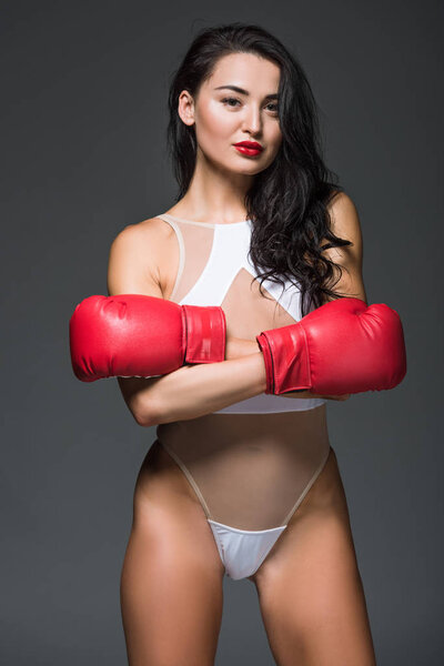 sexy sportive woman in white sportswear and boxing gloves standing with crossed arms isolated on grey 