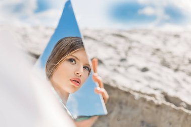charming girl holding piece of mirror and looking on her reflection clipart