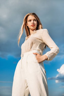 şık bir moda model ile bulutlu gökyüzü arka plan üzerinde beyaz şık giysiler içinde poz, alttan görünüm