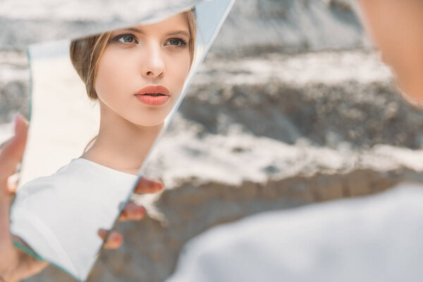 elegant blonde girl holding piece of mirror and looking on her reflection