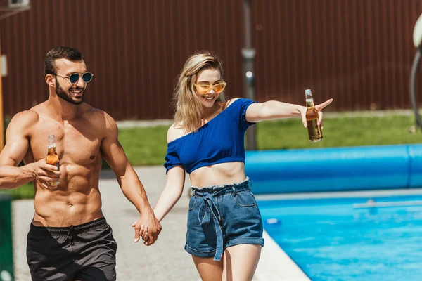 Happy Couple Bottles Beer Holding Hands Girl Pointing Poolside — Stock Photo, Image