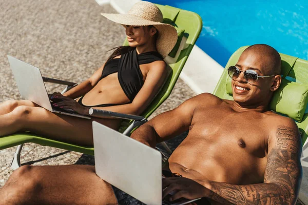 Interracial Couple Relaxing Sunbeds Using Laptops Poolside — Stock Photo, Image