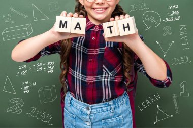 cropped image of schoolchild holding wooden cubes with word math near blackboard with mathematics symbols clipart