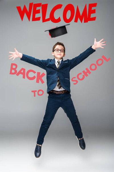 schoolboy in graduation cap jumping, isolated on grey with "welcome back to school" lettering