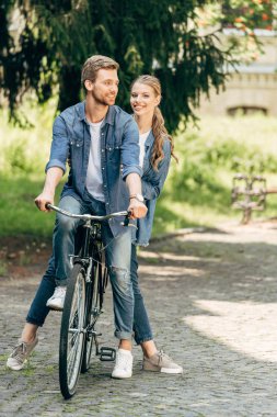 beautiful young couple riding vintage bicycle together at park clipart