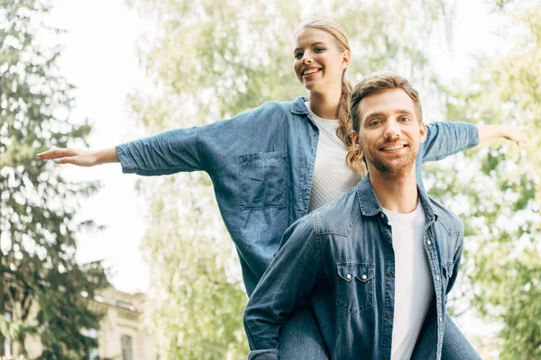 Leende Ung Kvinna Åka Snålskjuts Hennes Pojkvän Park — Stockfoto